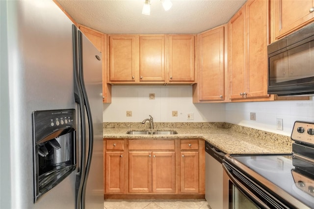 kitchen with light tile patterned flooring, appliances with stainless steel finishes, a textured ceiling, light stone countertops, and sink