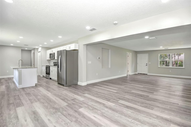 kitchen with white cabinets, stainless steel appliances, a kitchen island with sink, and light hardwood / wood-style flooring