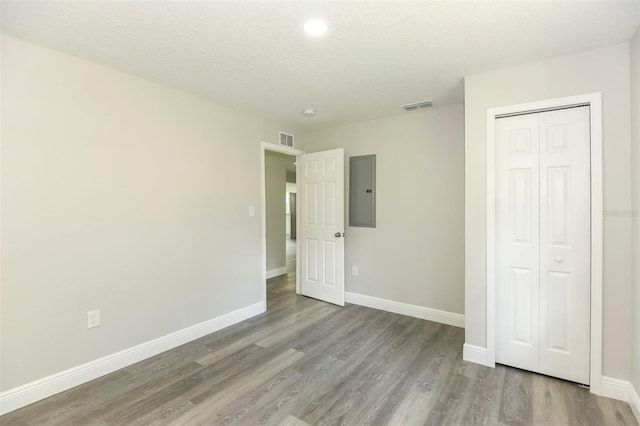 unfurnished bedroom with electric panel, a closet, light hardwood / wood-style floors, and a textured ceiling