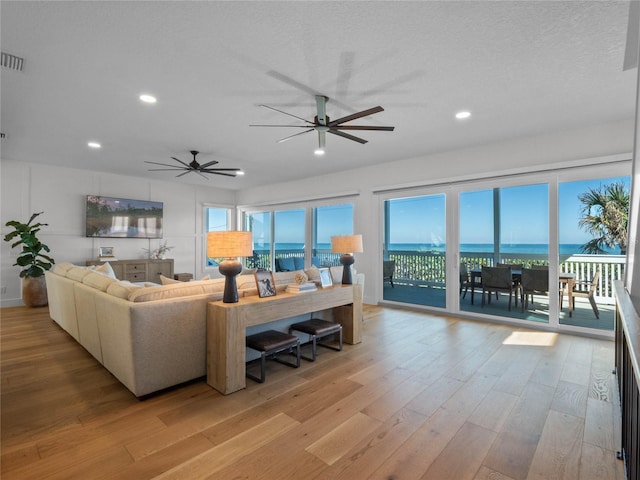 living room featuring a textured ceiling, a water view, light hardwood / wood-style flooring, and ceiling fan