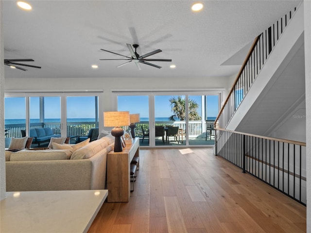 living room with ceiling fan, a textured ceiling, light hardwood / wood-style flooring, and a water view