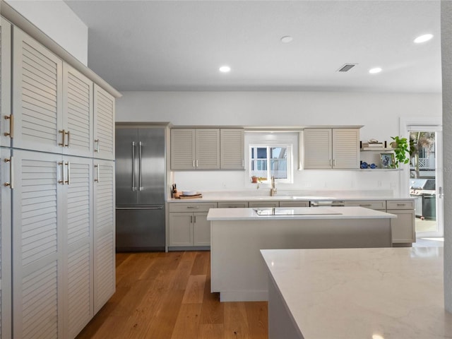 kitchen featuring sink, light stone countertops, gray cabinets, hardwood / wood-style floors, and built in fridge