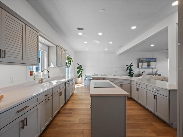 kitchen with light hardwood / wood-style flooring, sink, a kitchen island with sink, gray cabinetry, and black electric cooktop