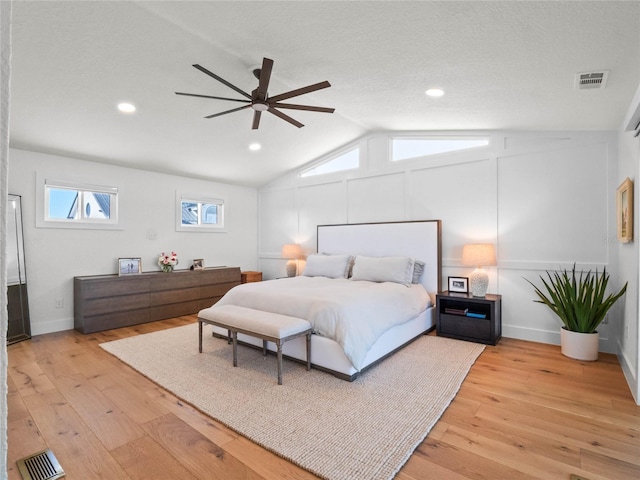 bedroom with ceiling fan, light hardwood / wood-style flooring, vaulted ceiling, and a textured ceiling