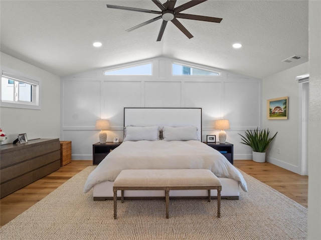 bedroom featuring ceiling fan, light hardwood / wood-style floors, a textured ceiling, and lofted ceiling