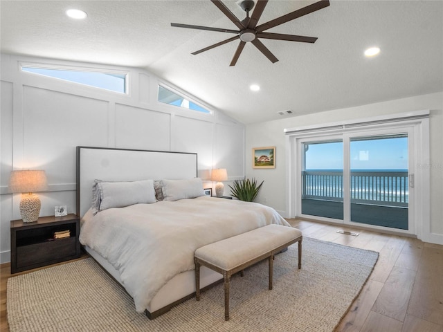 bedroom featuring lofted ceiling, light hardwood / wood-style floors, access to outside, a water view, and ceiling fan