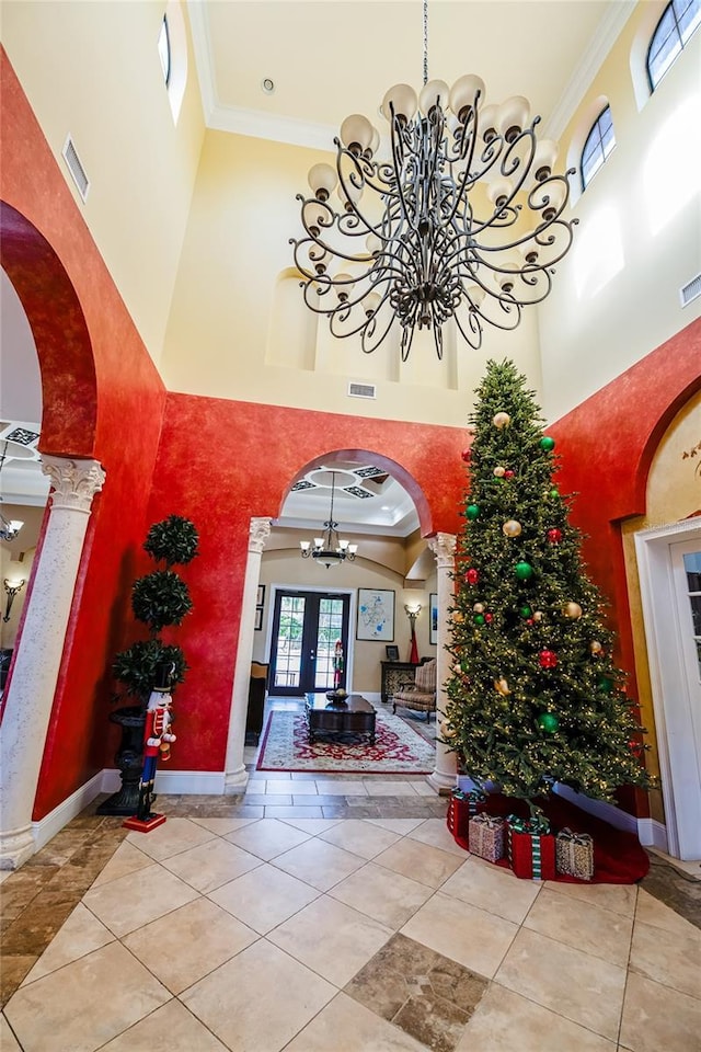 entryway with ornate columns, french doors, a towering ceiling, and ornamental molding