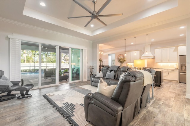 living room with a tray ceiling, ceiling fan, crown molding, and light hardwood / wood-style floors