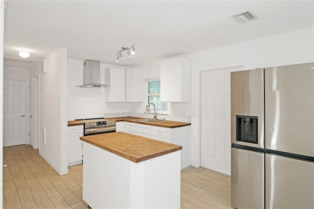 kitchen with a center island, wooden counters, white cabinets, wall chimney range hood, and appliances with stainless steel finishes