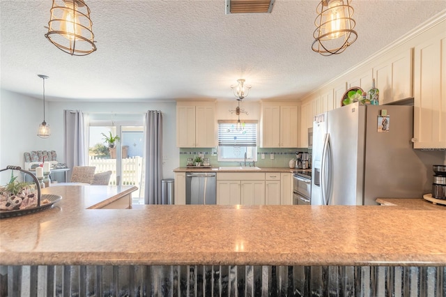 kitchen with sink, tasteful backsplash, pendant lighting, a textured ceiling, and appliances with stainless steel finishes