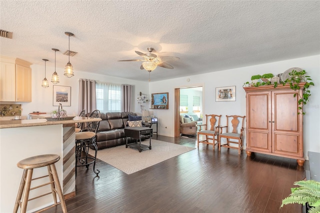 living room with a textured ceiling, ceiling fan, and dark wood-type flooring