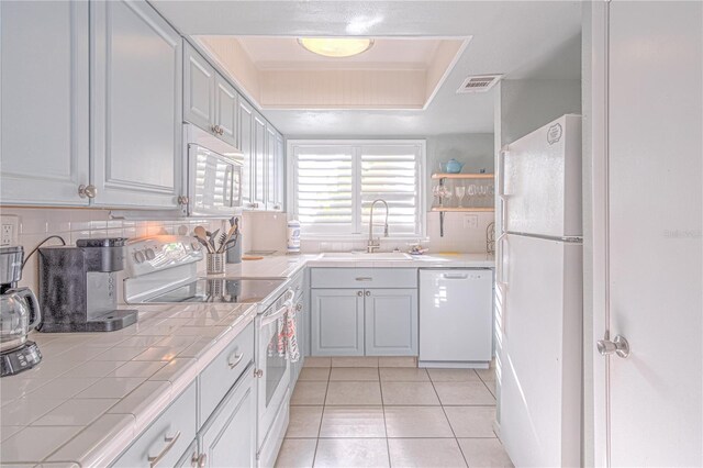 4017 Saxon Dr, New Smyrna Beach, FL 32169 - kitchen with white appliances, tile countertops, a raised ceiling, and light tile patterned floors