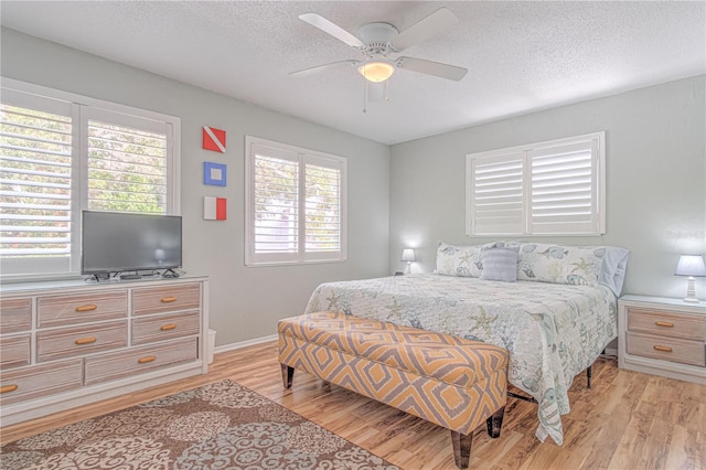 bedroom featuring ceiling fan, light wood-type flooring, a textured ceiling, and multiple windows