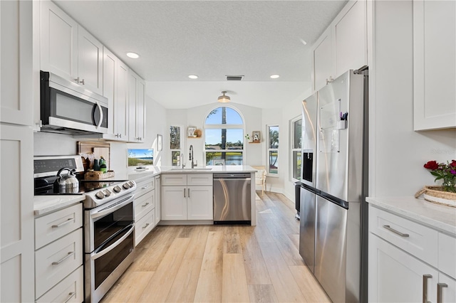 kitchen with white cabinets, vaulted ceiling, light stone countertops, appliances with stainless steel finishes, and kitchen peninsula