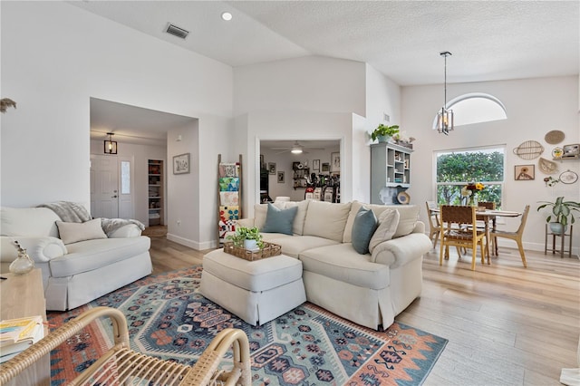 living room with a textured ceiling, ceiling fan with notable chandelier, high vaulted ceiling, and light hardwood / wood-style flooring