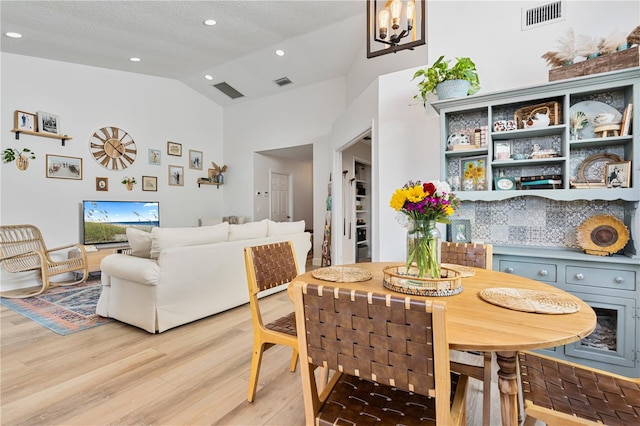 dining space featuring light wood-type flooring, a textured ceiling, high vaulted ceiling, and a chandelier