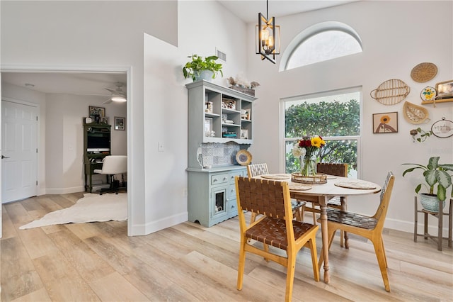 dining room with ceiling fan with notable chandelier, light wood-type flooring, and a high ceiling