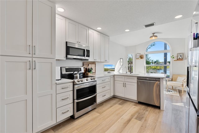 kitchen featuring kitchen peninsula, a textured ceiling, vaulted ceiling, white cabinets, and appliances with stainless steel finishes