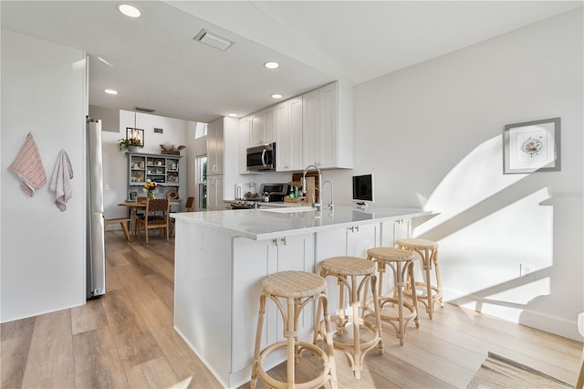 kitchen with a breakfast bar, white cabinets, light hardwood / wood-style flooring, appliances with stainless steel finishes, and kitchen peninsula