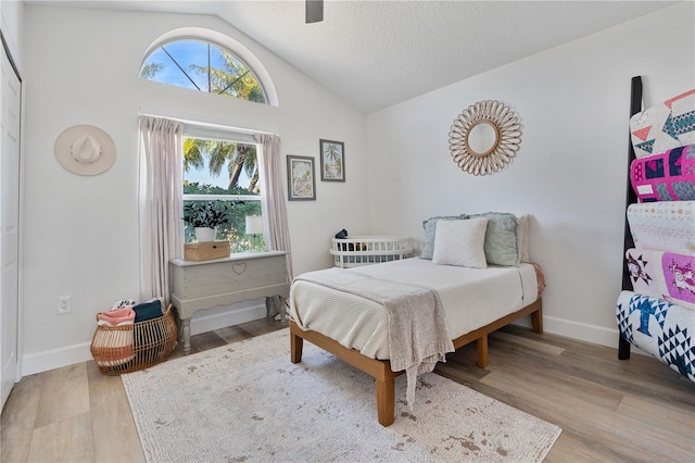 bedroom with a textured ceiling, ceiling fan, light hardwood / wood-style floors, and vaulted ceiling