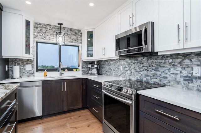 kitchen featuring dark brown cabinetry, stainless steel appliances, white cabinets, light hardwood / wood-style floors, and hanging light fixtures