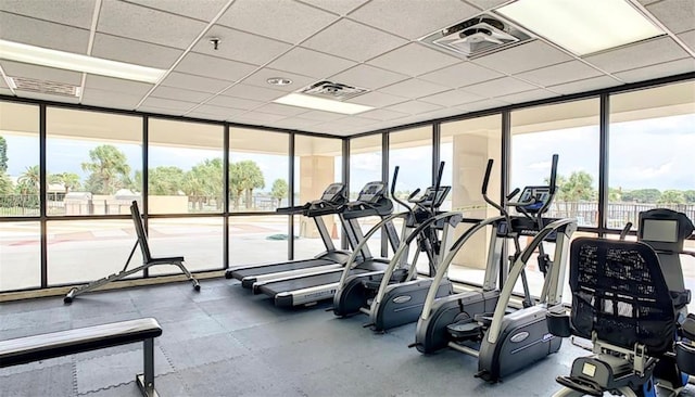 gym with a paneled ceiling, expansive windows, and a healthy amount of sunlight