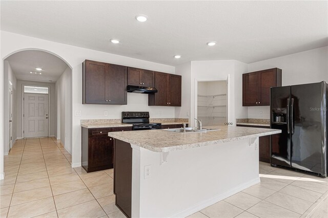 kitchen with a breakfast bar, an island with sink, sink, black appliances, and dark brown cabinets