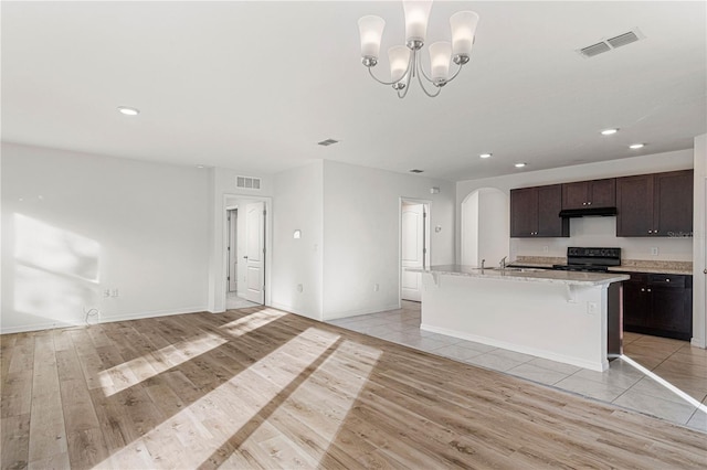 kitchen with dark brown cabinetry, a kitchen bar, light wood-type flooring, an island with sink, and black range with electric cooktop