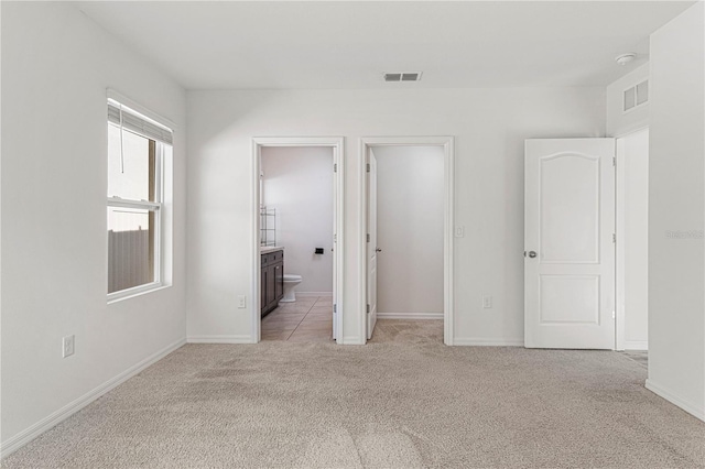 unfurnished bedroom featuring light colored carpet and ensuite bathroom