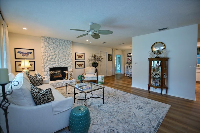 living room featuring a fireplace, a textured ceiling, dark hardwood / wood-style floors, and ceiling fan