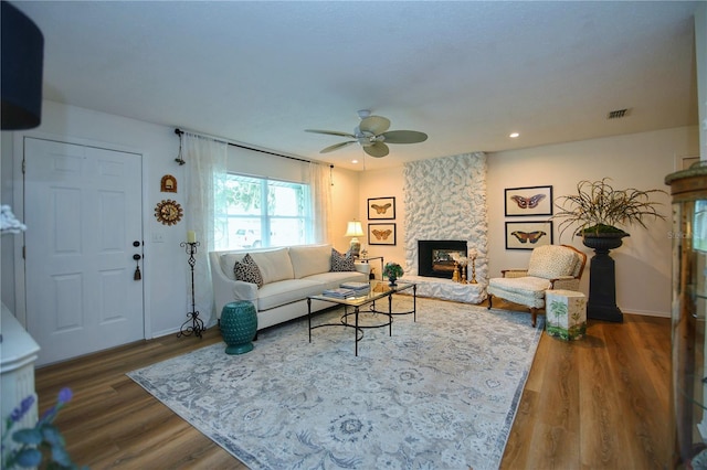 living room with dark hardwood / wood-style floors, ceiling fan, and a stone fireplace