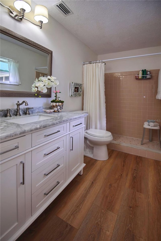 bathroom featuring vanity, hardwood / wood-style flooring, toilet, walk in shower, and a textured ceiling