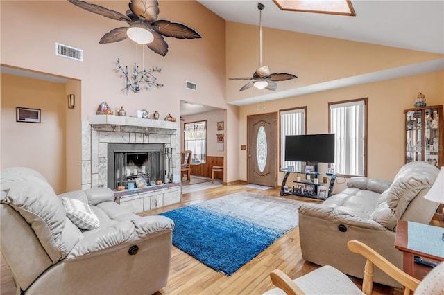 living room with a tile fireplace, light wood-type flooring, and high vaulted ceiling