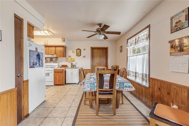 dining space featuring ceiling fan, light tile patterned floors, and wooden walls