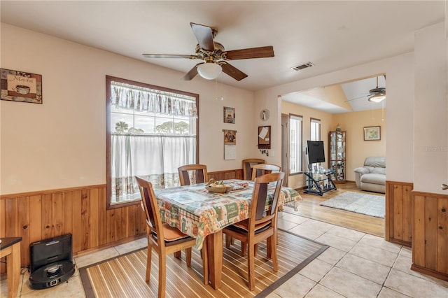 dining area with light hardwood / wood-style flooring, plenty of natural light, wood walls, and ceiling fan