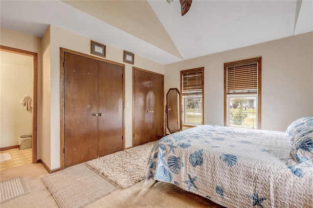 bedroom with vaulted ceiling, ensuite bath, light carpet, and two closets