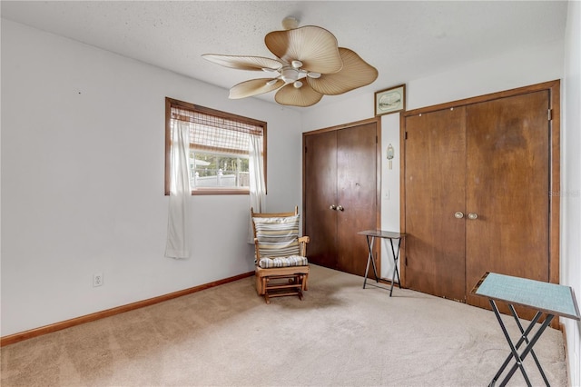 living area featuring ceiling fan, carpet floors, and a textured ceiling