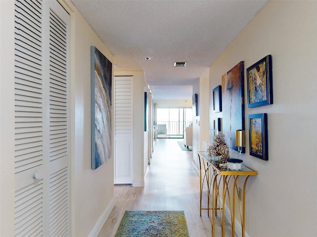 corridor with a textured ceiling and light wood-type flooring