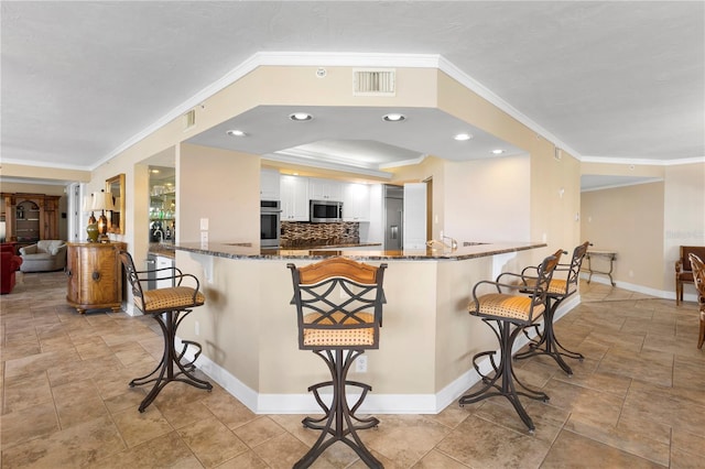 kitchen with stainless steel appliances, kitchen peninsula, a kitchen breakfast bar, and dark stone counters