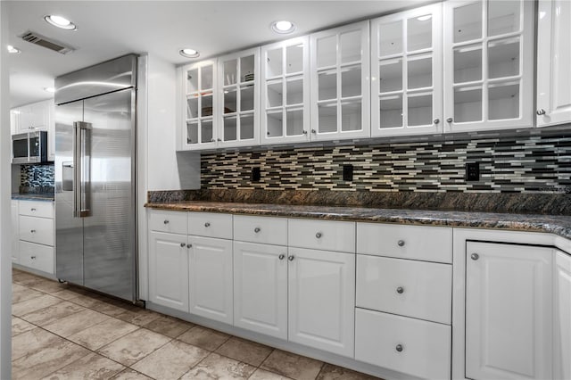 kitchen featuring decorative backsplash, dark stone counters, white cabinets, and appliances with stainless steel finishes