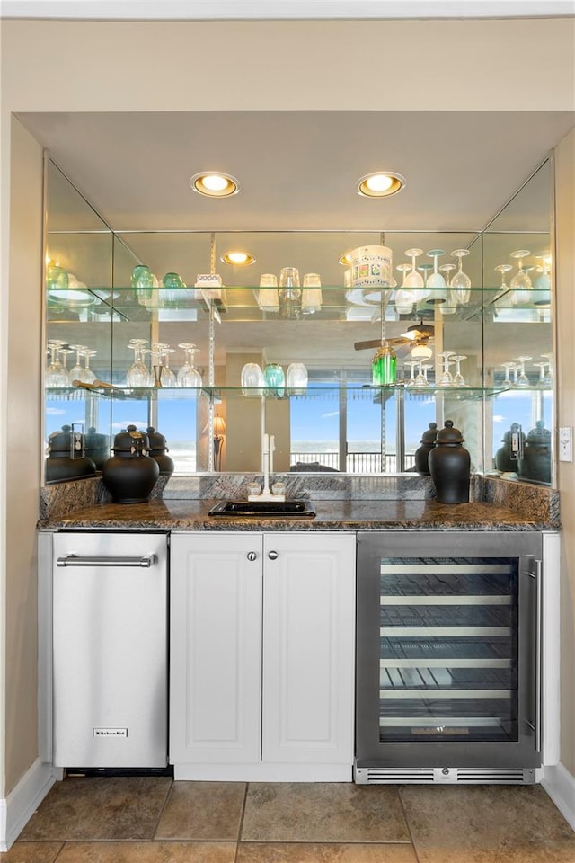 bar with wine cooler, white cabinetry, sink, and dark stone countertops