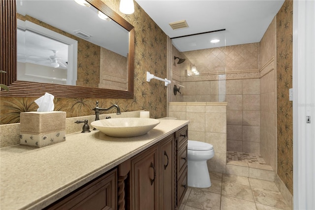 bathroom featuring vanity, tiled shower, ceiling fan, and toilet