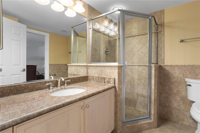 bathroom with vanity, toilet, a shower with door, and tile walls