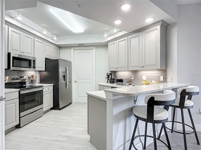 kitchen featuring tasteful backsplash, a tray ceiling, a breakfast bar, and appliances with stainless steel finishes