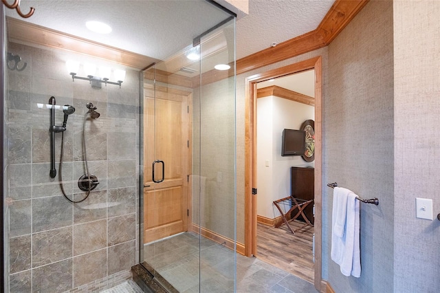 bathroom with a textured ceiling, hardwood / wood-style flooring, an enclosed shower, and ornamental molding