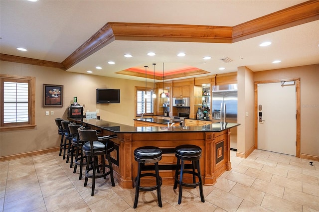 kitchen with kitchen peninsula, stainless steel appliances, a raised ceiling, hanging light fixtures, and a breakfast bar area