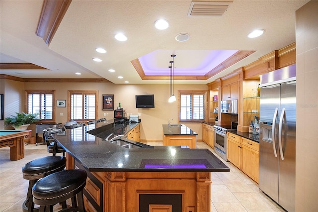 kitchen featuring kitchen peninsula, stainless steel appliances, a tray ceiling, sink, and hanging light fixtures