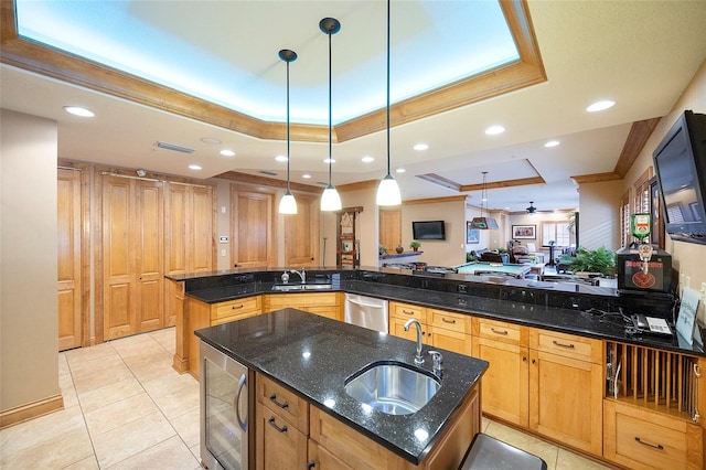 kitchen featuring ceiling fan, hanging light fixtures, dark stone counters, a tray ceiling, and a kitchen island with sink