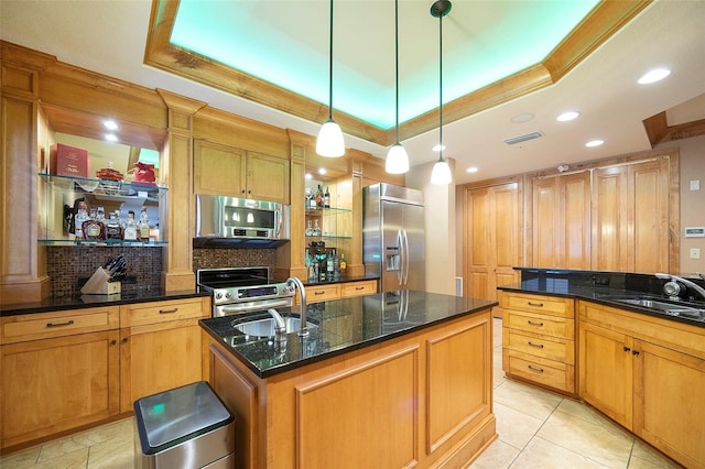 kitchen with sink, stainless steel appliances, a tray ceiling, and an island with sink