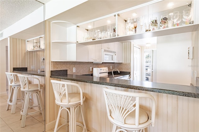 kitchen with light tile patterned floors, a kitchen breakfast bar, white appliances, decorative backsplash, and white cabinets